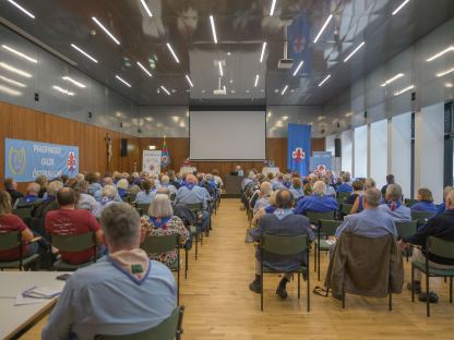 Viele Personen sittzen in einem Veranstaltungsraum und ören einem Redner zu.