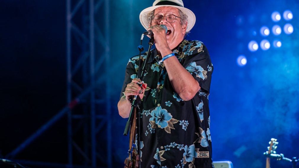 Ein Sänger einer Band mit einem Hut und einem Mikrofon auf der Bühne mit blauer Beleuchtung. (Foto: Christian Huber)