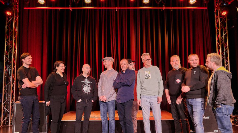 10 Mitarbeiter:innen vom Team vom Freiraum St. Pölten auf der Bühne vor rotem Vorhang. Foto: Klaus Engelmayer