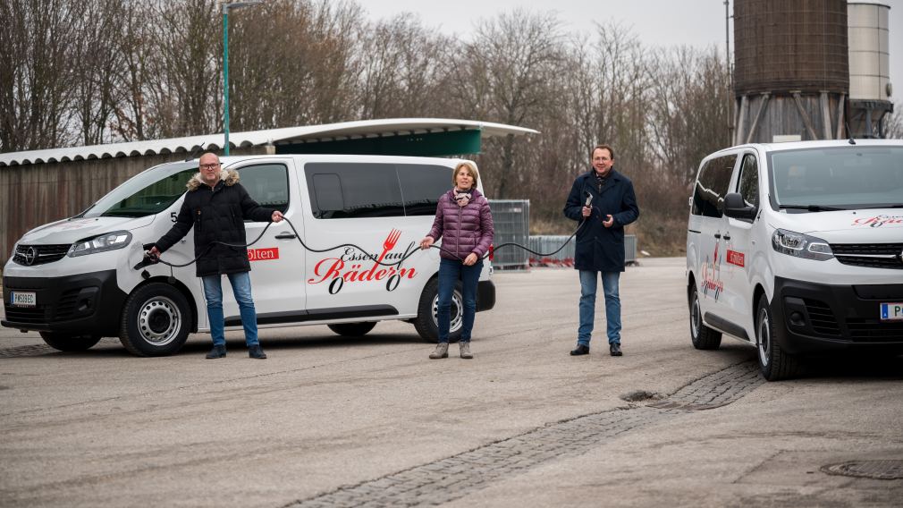 Drei Personen stehen neben den neuen Elektro-Busen von Essen auf Rädern und halten ein Auflagekabel in der Hand, das mit dem Stecker am Auto angeschlossen ist.